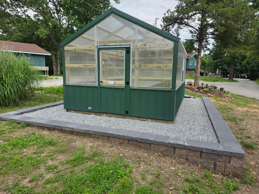 Greenhouse set on a gravel pad with retaining blocks around the base