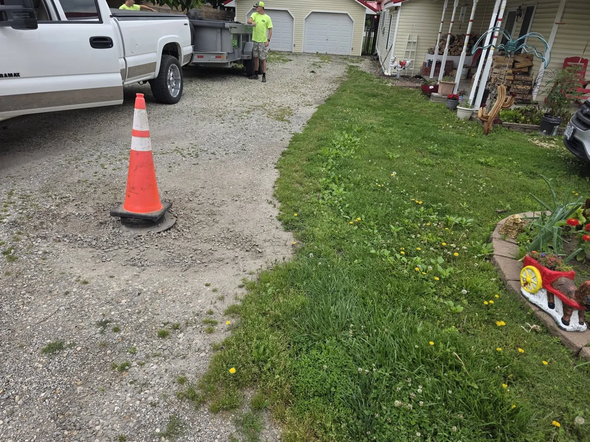 Before photo of a worn gravel driveway with grass and rough areas near a porch